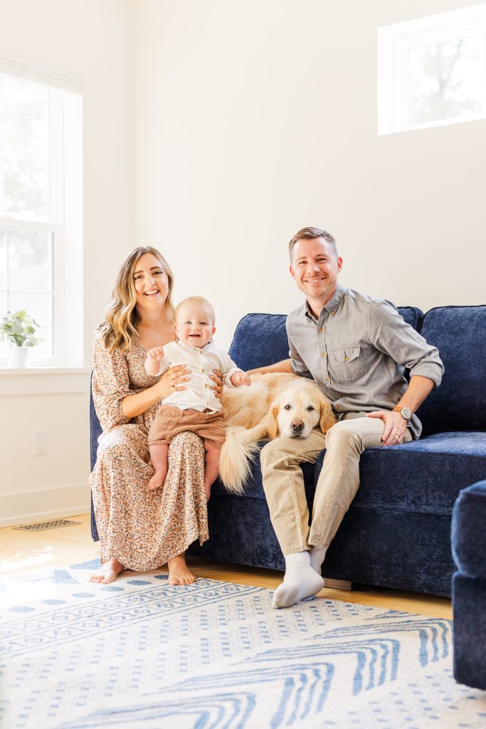 Family of mom, dad, baby, and dog sitting together in their living room, smiling at the camera during a day training session with Dogology University