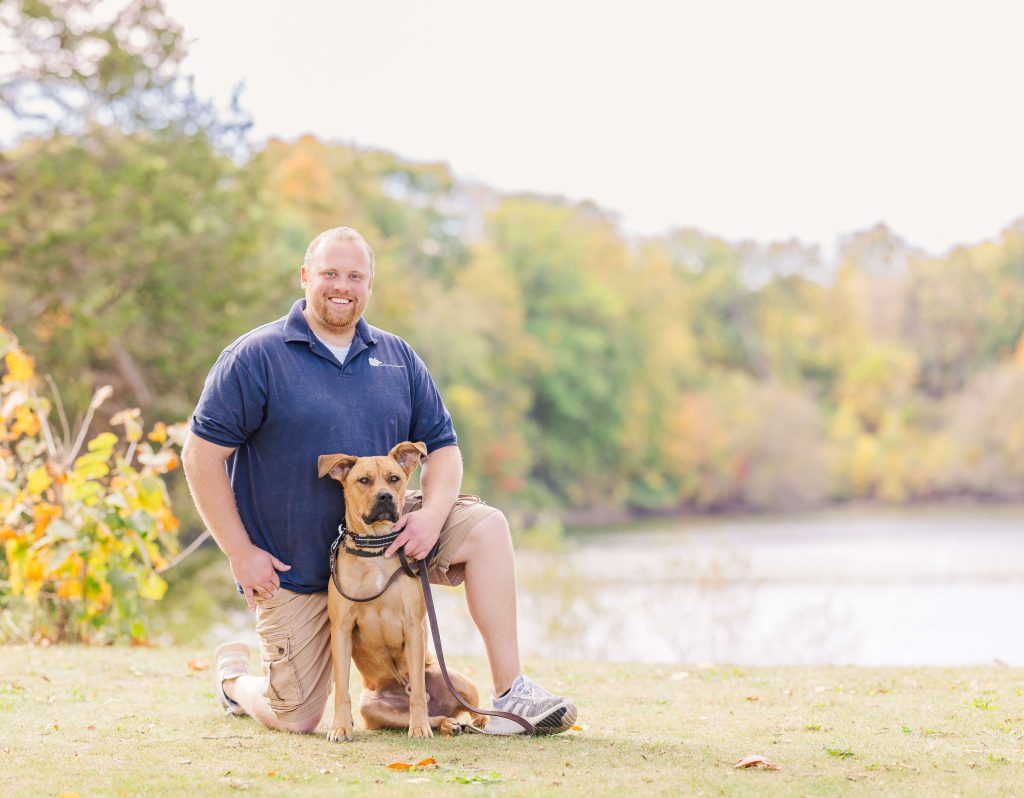 Matthew Lamarand kneeling with a tan dog smiling at the camera at Newburgh Point in Livonia, MI, practicing real-world training for a previously reactive dog
