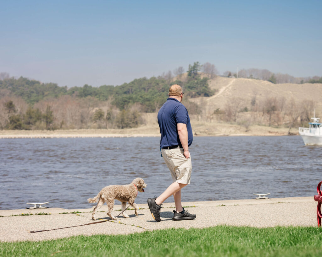Dog walking calmly beside a trainer on a boardwalk during off-leash dog training in Grand Haven, MI.